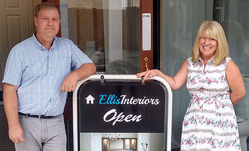 A photo of owners David and Jane stood outside the showroom entrance either side of their advertisement board on a sunny day.