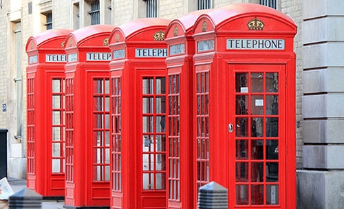 Five red telephone boxes next to each other backing onto a building.