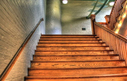 A natural wood staircase climbing up through a white bricked house.